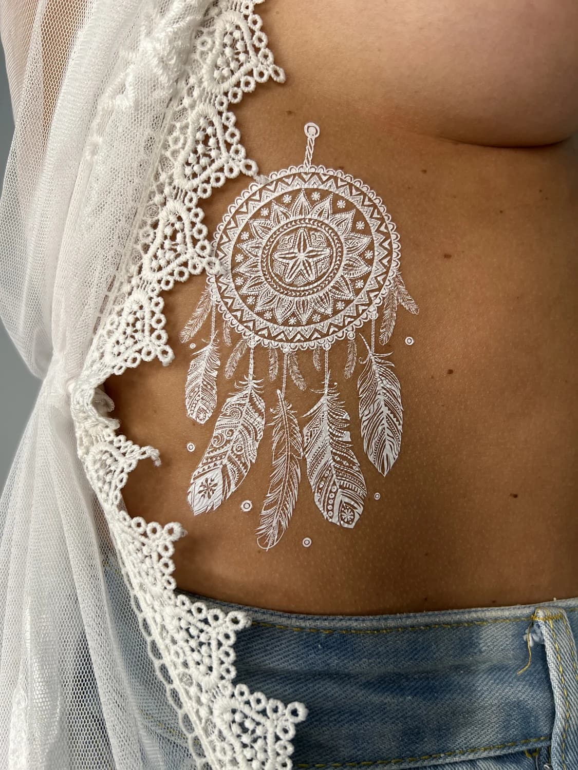 White-ink dreamcatcher across the ribs beside lace