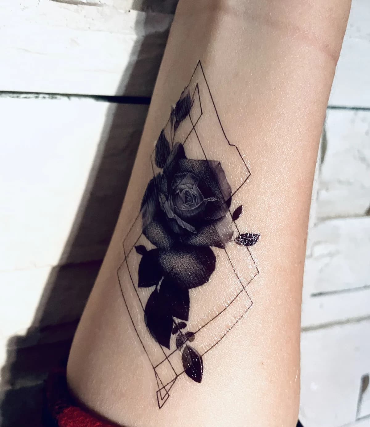 Black-and-grey rose framed in fine geometric lines on a forearm