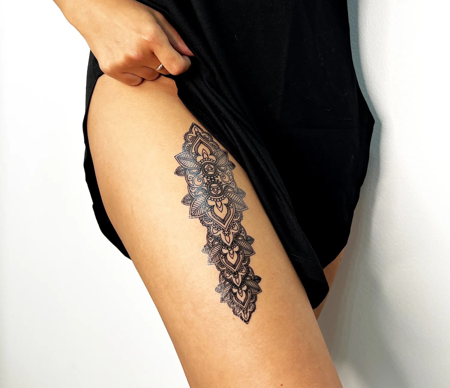 Ornamental mandala tattoo down the thigh beside a black dress